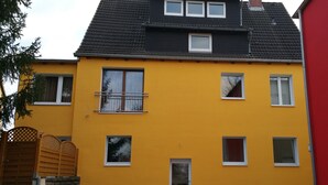Een gebouw met twee verdiepingen, een gele gevel, meerdere ramen en een zwart dak.