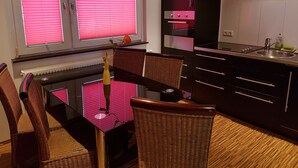 Een moderne keuken met een eethoek, bestaande uit een zwart kastje, een spoelbak en een eettafel met stoelen.