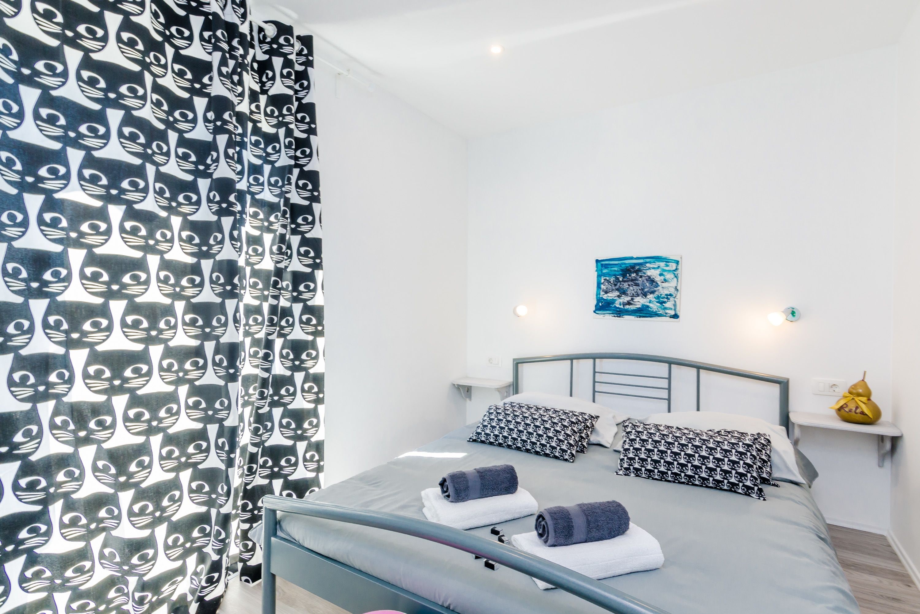 A neatly made bed with patterned pillows and a blue artwork on the wall.