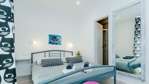 A modern bedroom with a bed, a colorful stool, a large mirror, and a small artwork on the wall. - Guest House Nikolina (Dubrovnik)