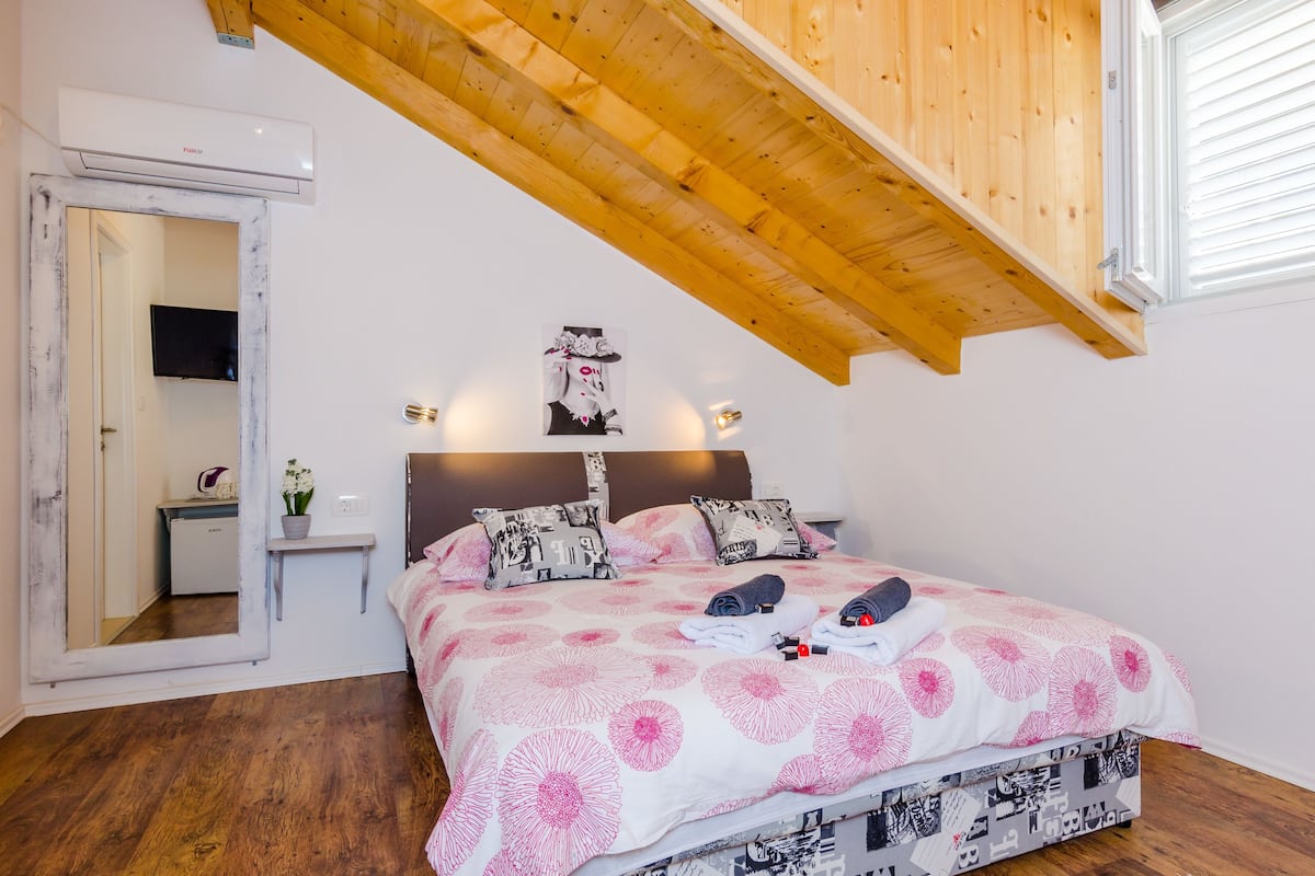 Une chambre à coucher avec un lit, des poutres en bois au plafond, un climatiseur fixé au mur, une table de chevet avec une lampe et un miroir.