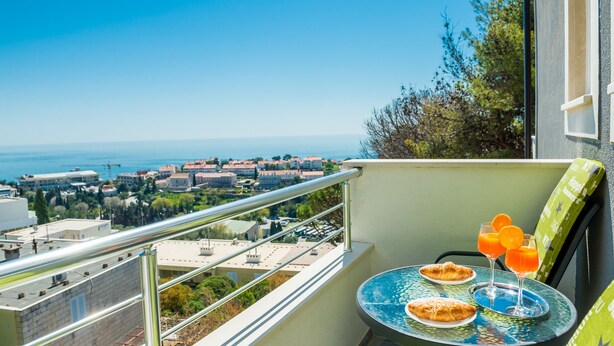 A balcony with a table set for two, overlooking a coastal cityscape. - Guest House Nikolina (Dubrovnik)