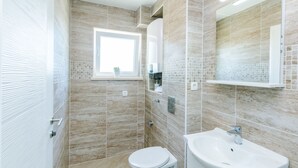 A modern bathroom with beige tiles, a white toilet, a sink, and a window. - Guest House Nikolina (Dubrovnik)