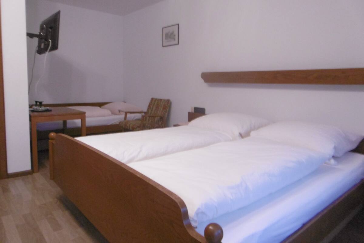 Une chambre à coucher avec un lit en bois, une chaise, une table de chevet et un luminaire fixé au mur.