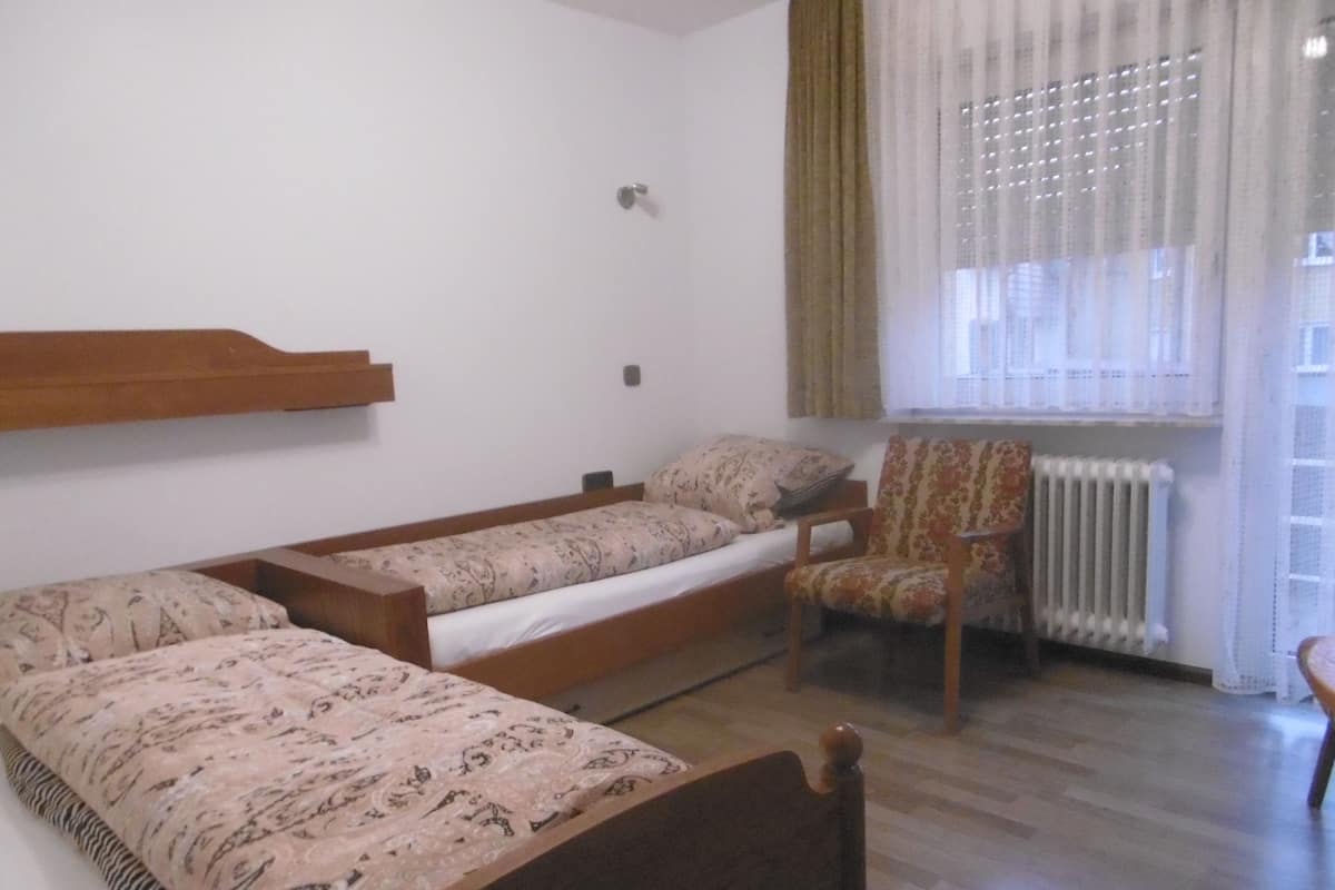 Une petite pièce simple, avec un lit en bois, une chaise et un radiateur.