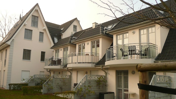 A row of three-story houses with balconies, a stone staircase, and a small garden area. - Antonia Rerik (Rerik)