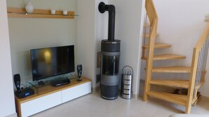 A living room with a TV, a black heater, a trash bin, and a wooden staircase. - Antonia Rerik (Rerik)