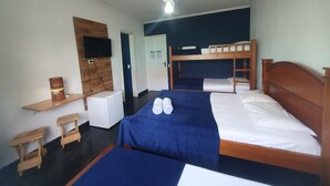 Habitación de hotel con literas, un escritorio, una silla, un televisor y un ventilador de techo.