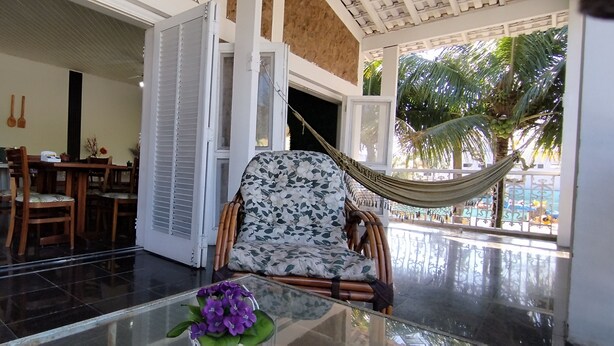 Una habitación amplia con zona de comedor, una silla hamaca y vistas a palmeras.