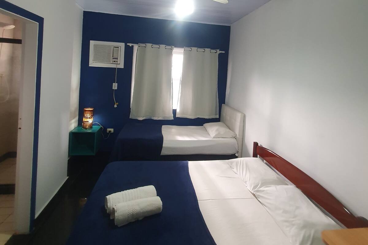 Habitación de hotel con dos camas, un ventilador de techo, una mesita de noche con lámpara y una ventana con cortinas.