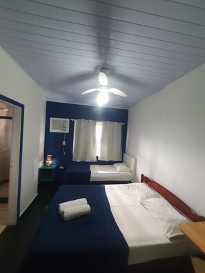 A hotel room with two beds, a ceiling fan, a bedside table with a lamp, and a window with curtains. - Pousada Canto dos Mares (Guarujá)