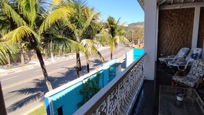 Balcón con vista a una carretera y palmeras, una piscina y dos sillas de descanso con una mesa.