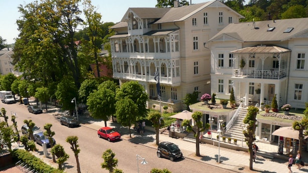 Une vue de rue avec un grand bâtiment doté de balcons et d’une fontaine.