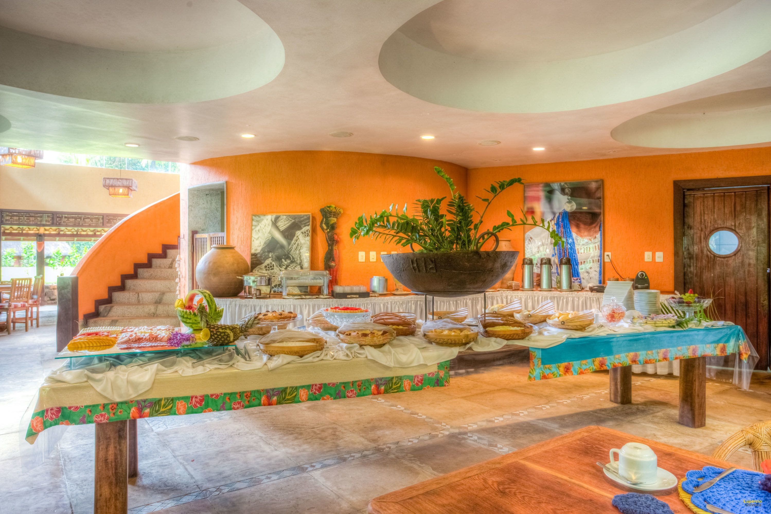 A spacious dining area with a central table featuring a large bowl, surrounded by various dishes and a decorative plant.