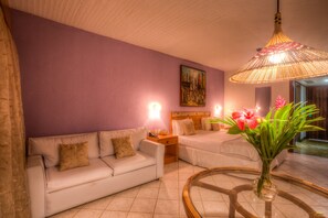 A hotel room with a purple wall, two beds, a white sofa, a glass coffee table, and a hanging lamp. - Itacaré Eco Resort (Itacaré)