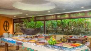 Montaje de bufé con diferentes opciones de comida y una maceta grande con plantas tropicales.