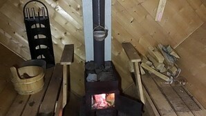 Ein rustikaler Holzraum mit Kaminofen, Bänken und einem Metallregal.