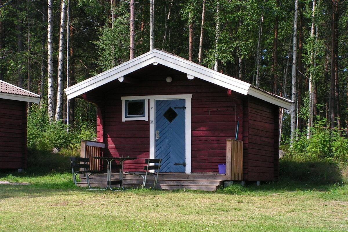 Una cabaña pequeña con una puerta azul, un porche con dos sillas y una ventana.