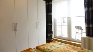 Un dormitorio con un armario amplio, una ventana con cortinas y vistas al balcón exterior.