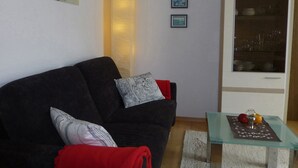 Una sala de estar con un sofá oscuro, una mesa de centro de vidrio y un mueble con vajilla.