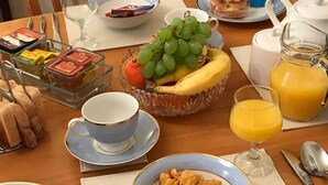 Ett frukostbord med en skål med flingor, ett glas apelsinjuice, en fruktskål med druvor och bananer, en kopp kaffe och ett glas mjölk.