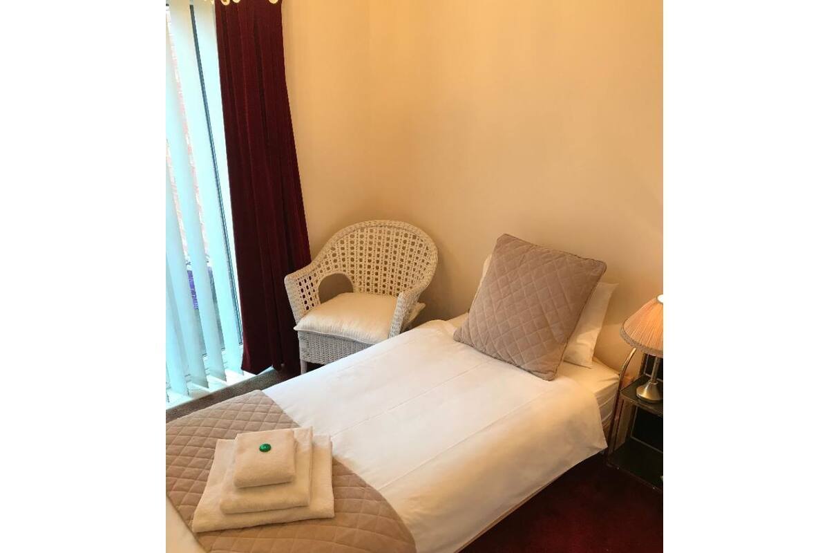 A hotel room with a bed, a chair, a nightstand, and a window with curtains.