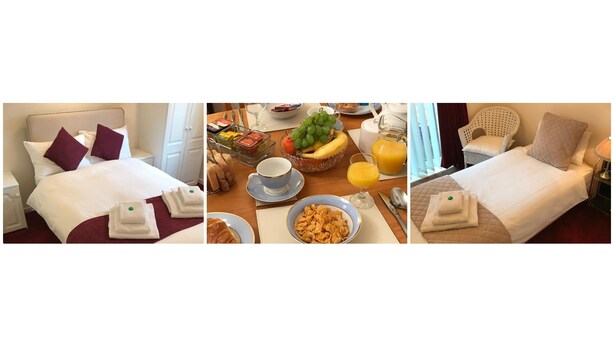 Ett hotellrum med en säng, ett frukostbord med frukt, en skål med flingor och ett glas juice.