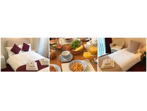 Quarto de hotel com cama, mesa de café da manhã com frutas, tigela de cereais e copo de suco.