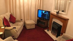 Ett vardagsrum med en beige soffgrupp, en tv, en öppen spis och en röd matta.