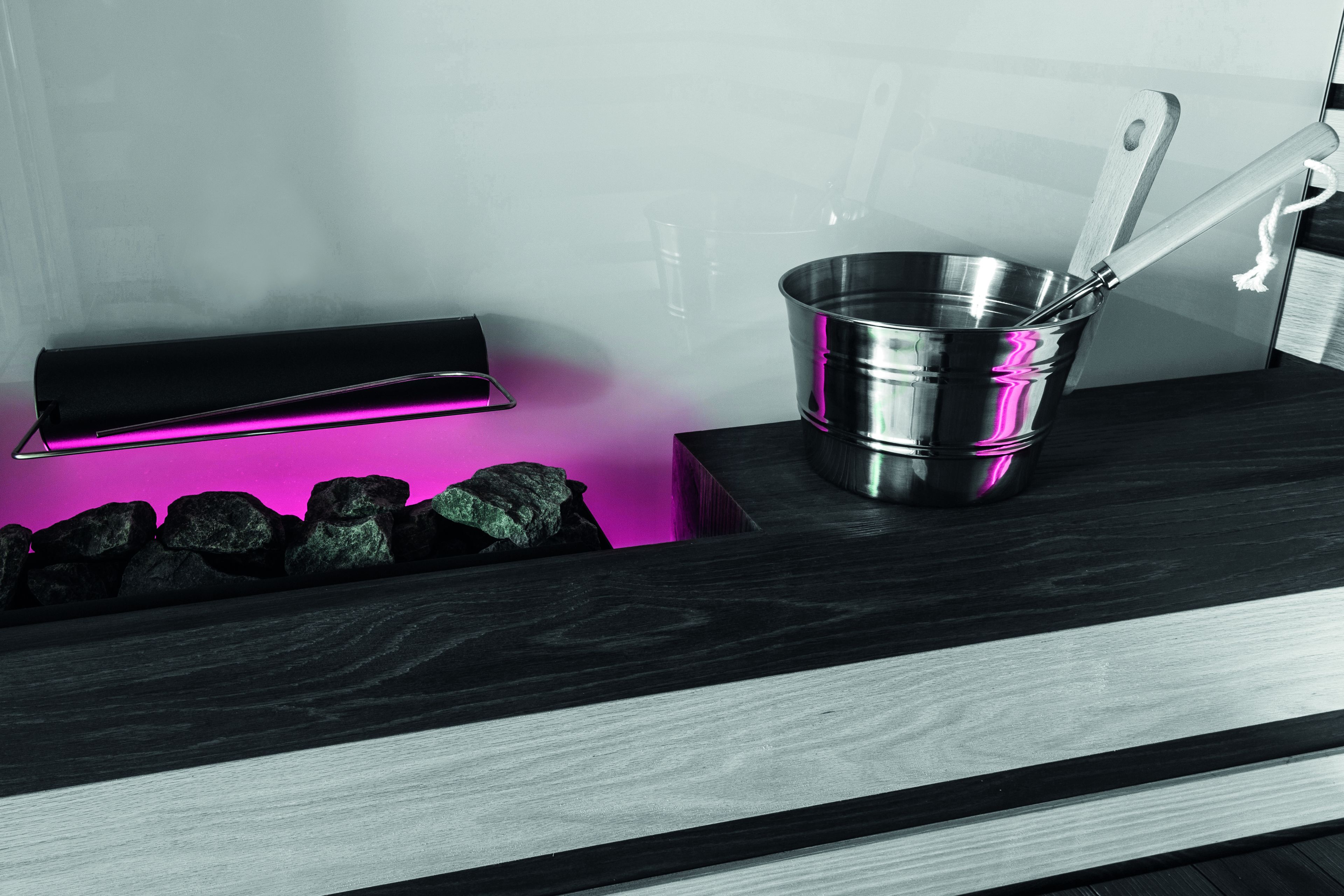 A kitchen counter with a stainless steel pot and a wooden spoon, a black box, and a pink light.