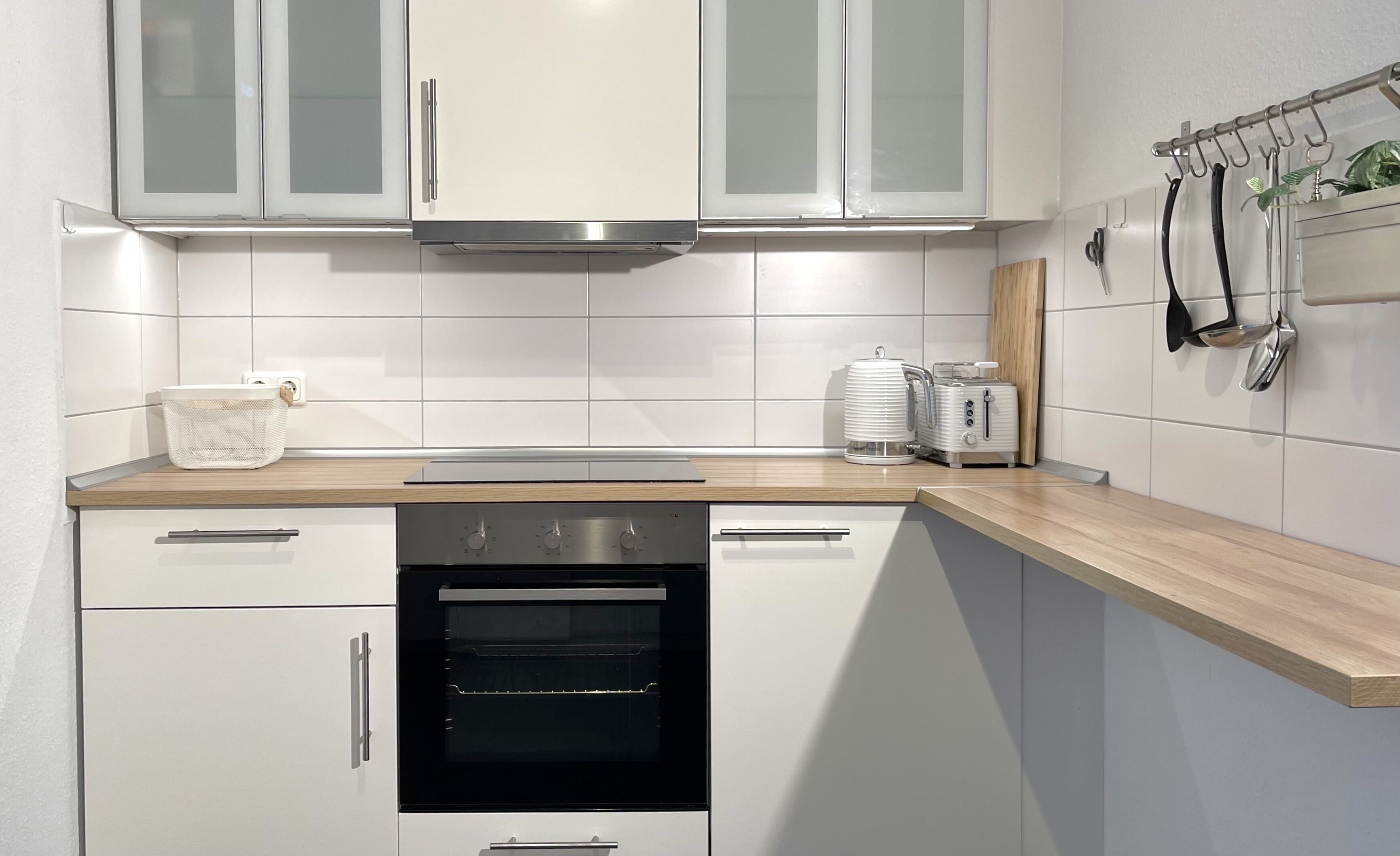 Una cucina moderna con mobili bianchi, una cappa aspirante in acciaio inossidabile, forno integrato e piano di lavoro in legno.
