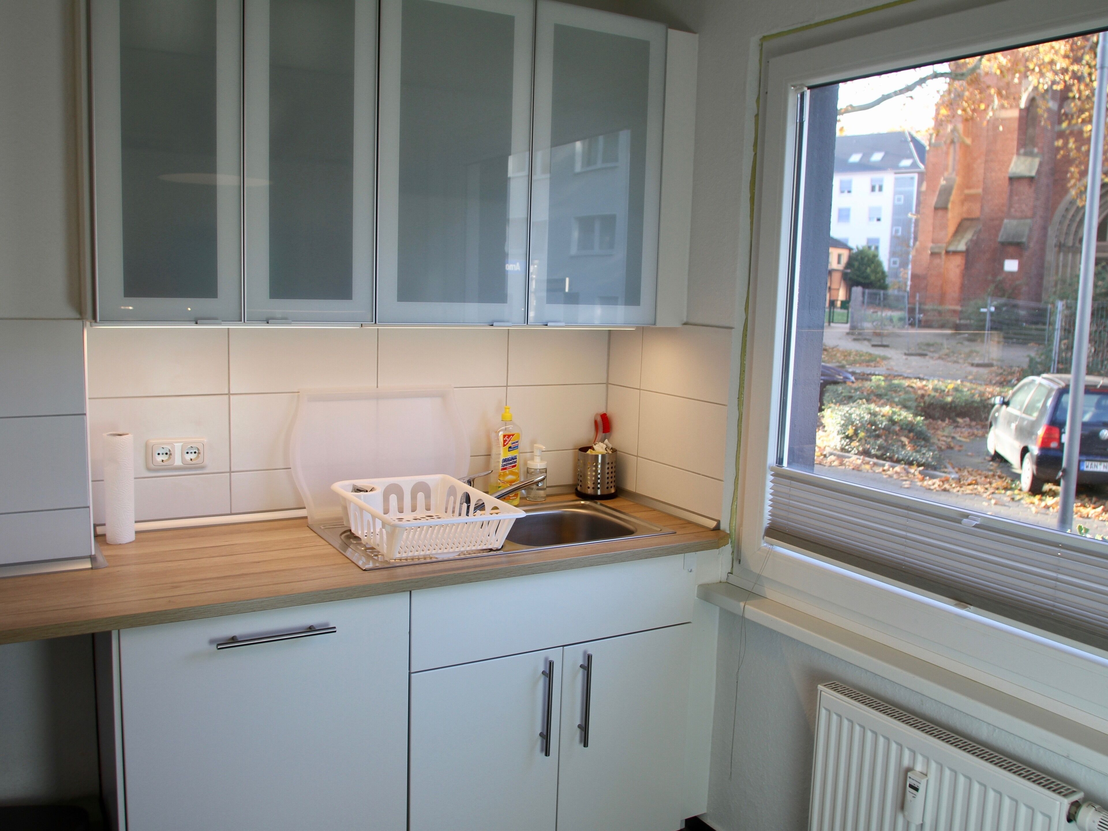 Een keuken met witte kastjes, een houten aanrecht, een spoelbak en een raam met uitzicht op een straat.