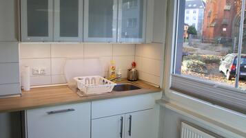 Een keuken met witte kastjes, een houten aanrecht, een spoelbak en een raam met uitzicht op een straat.