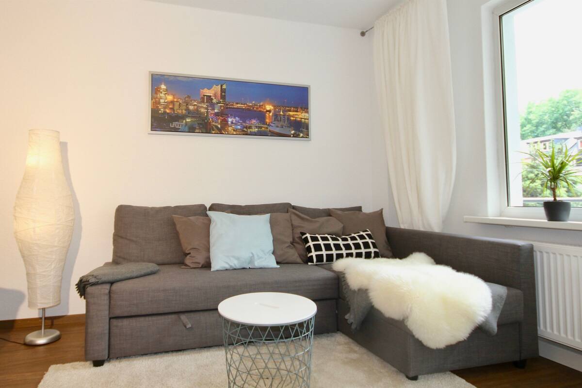 A living room with a grey sofa, a white round side table, and a cityscape painting on the wall.