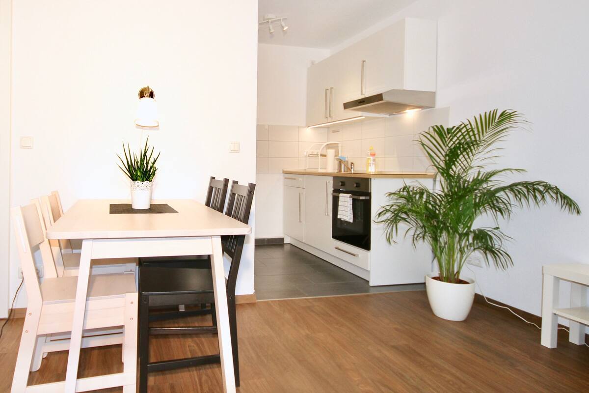 A modern kitchen with white cabinets, a built-in oven, and a dining area with a table and chairs.