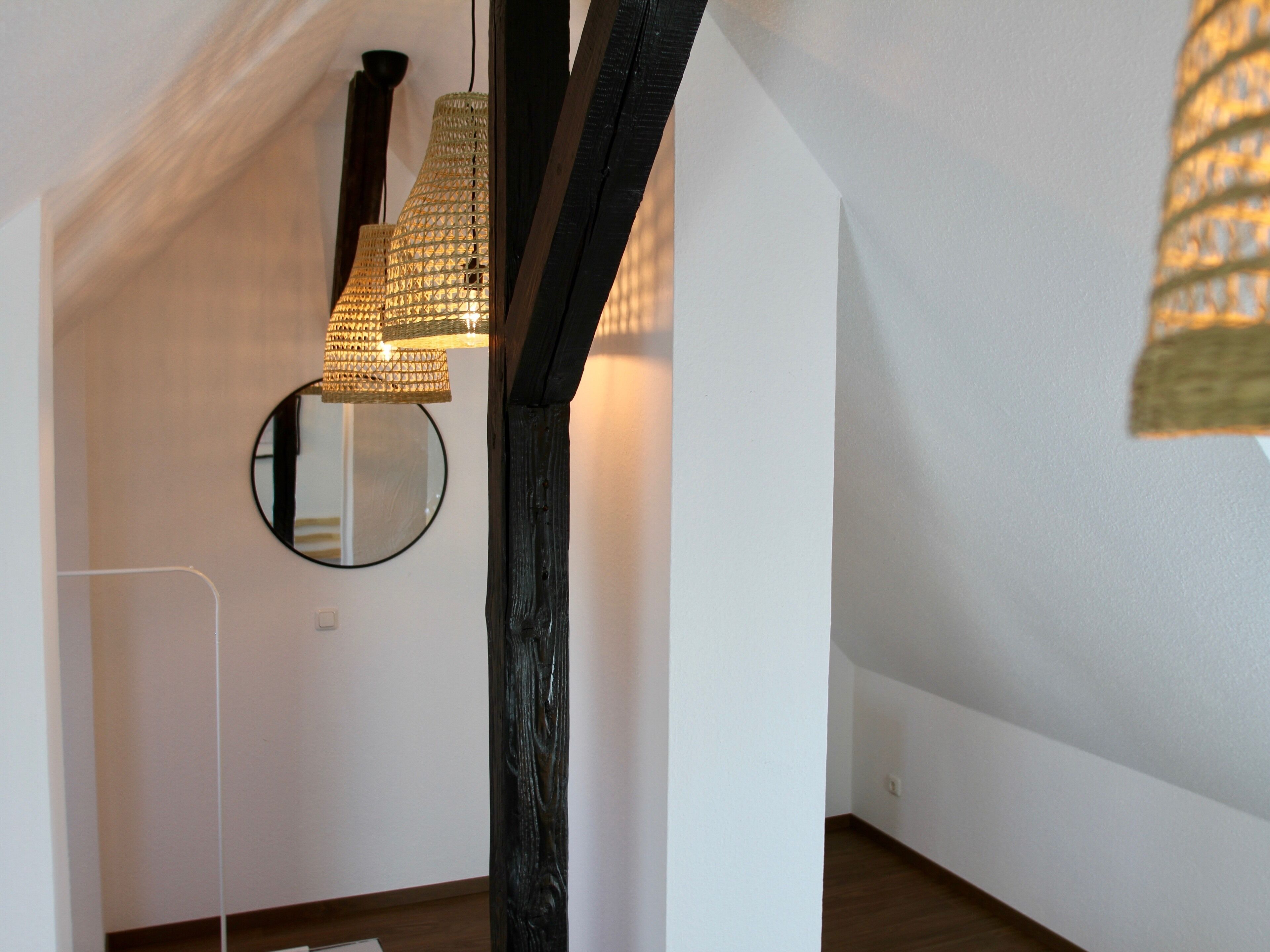 A room with exposed wooden beams, a round mirror, and a hanging light fixture.