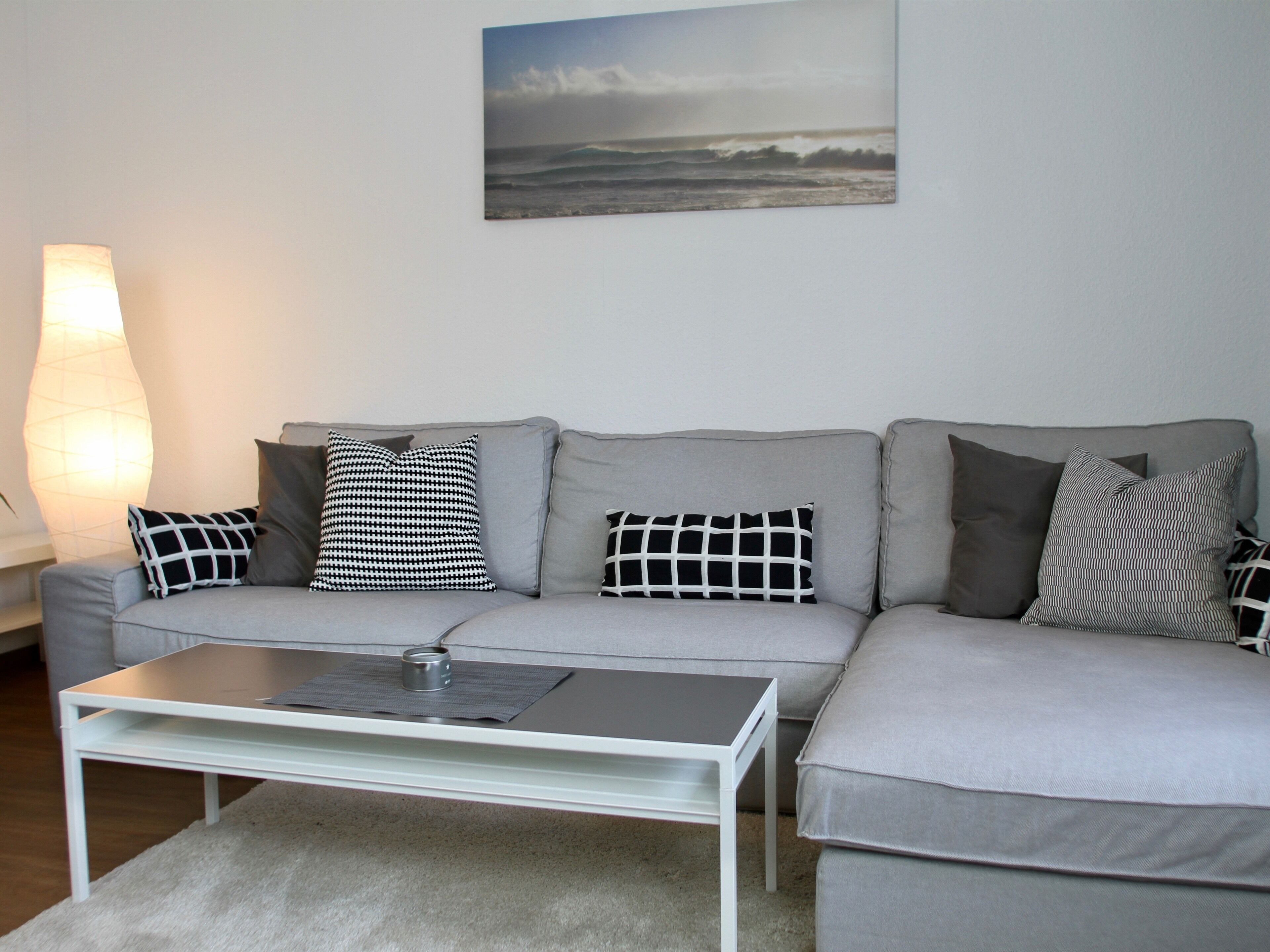 A grey sofa with patterned cushions, a white coffee table, and a large floor lamp.
