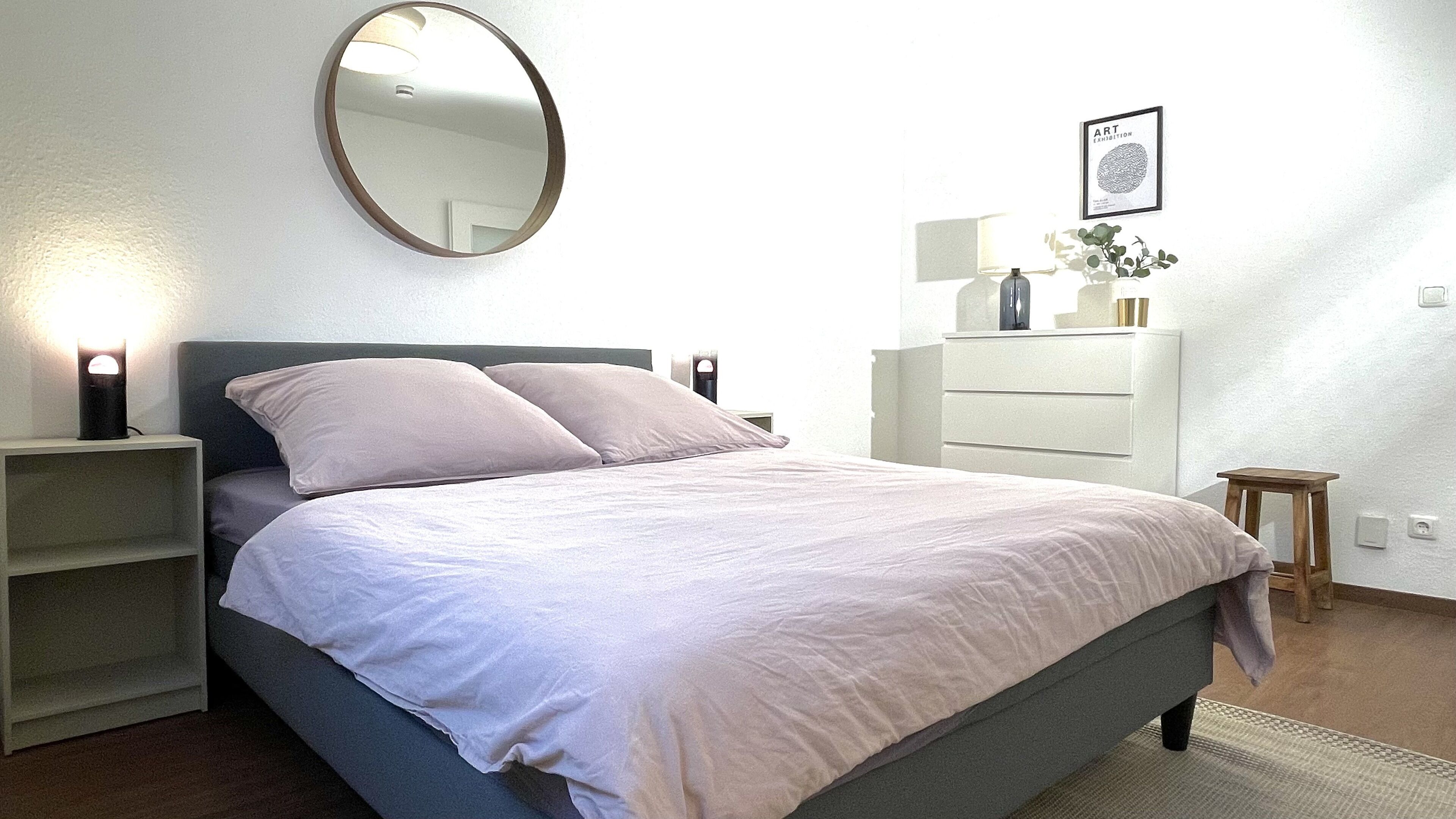 A bedroom with a bed, bedside tables, a dresser, a mirror, and a framed picture on the wall.