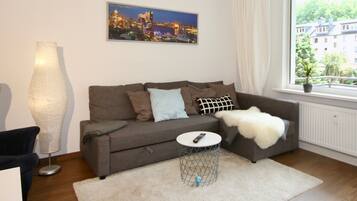 Een moderne woonkamer met een grijze bank, een witte plaid en een stadslandschap schilderij aan de muur.