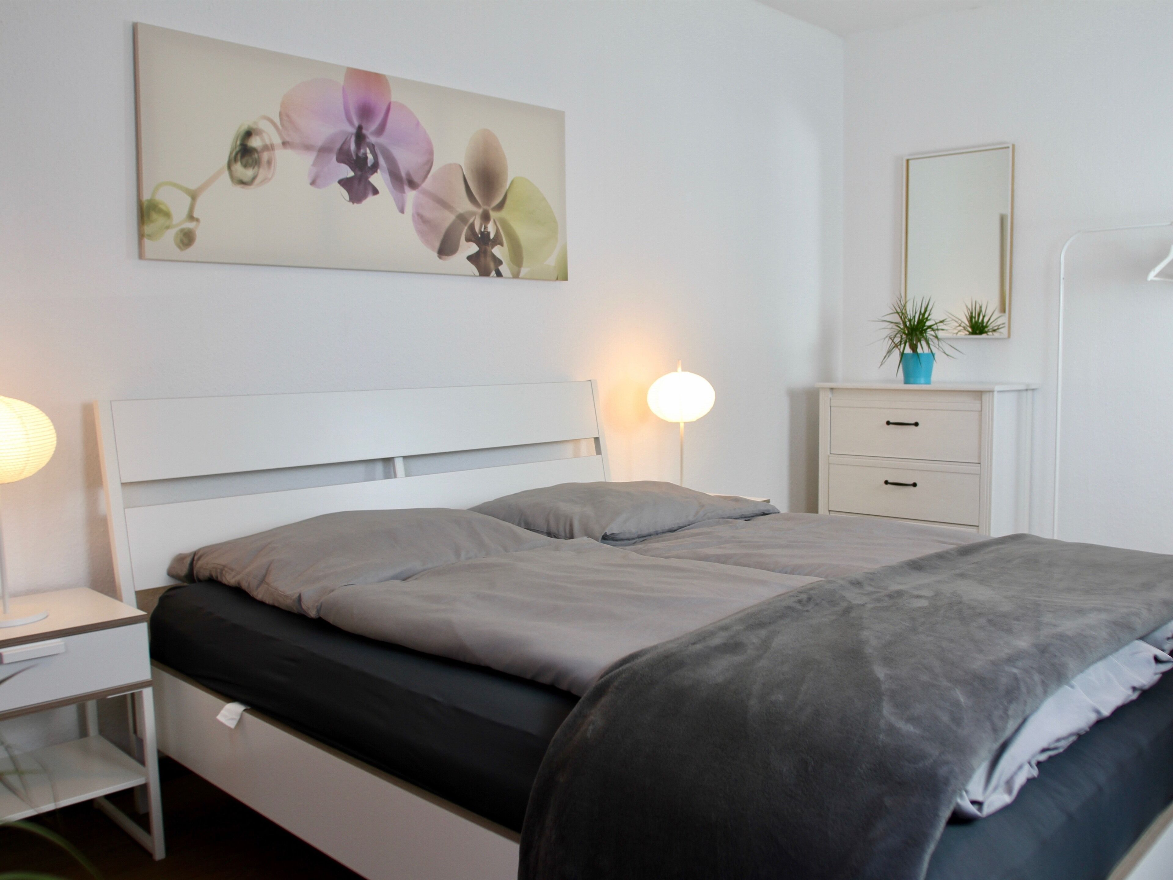 Un dormitorio con cama, mesitas de noche, cómoda, espejo y una obra de arte colgada en la pared.