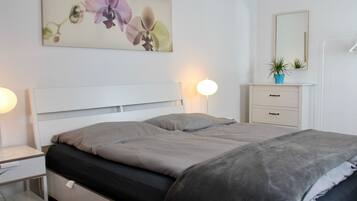 Un dormitorio con cama, mesitas de noche, cómoda, espejo y una obra de arte colgada en la pared.