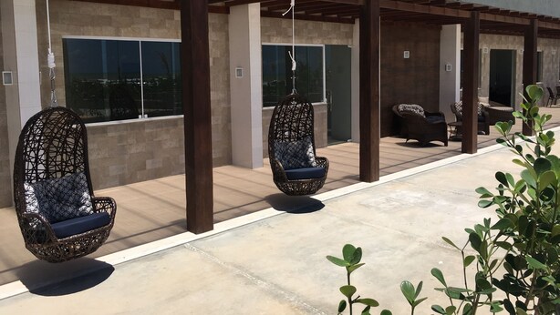 A modern outdoor seating area with wicker chairs and a hanging chair, a pool, and a Tropical Mar Hotel sign. - Tropical Mar Hotel (Aracaju)
