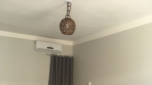 A neatly made bed with white linens in a room with a wooden headboard, a hanging woven light fixture, and a wall-mounted air conditioning unit. - Tropical Mar Hotel (Aracaju)