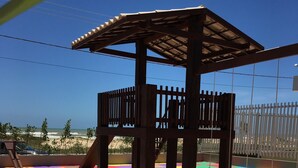 A wooden play structure with a roof, surrounded by colorful interlocking foam mats on a tiled patio. - Tropical Mar Hotel (Aracaju)