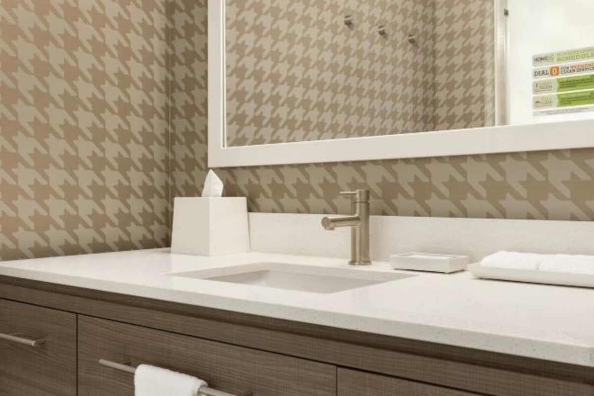 Ein modernes Badezimmer mit einer wandumschließenden Hundszahn-Musterung, einem weißen Waschbecken mit silbernem Wasserhahn und einem großen Spiegel darüber.