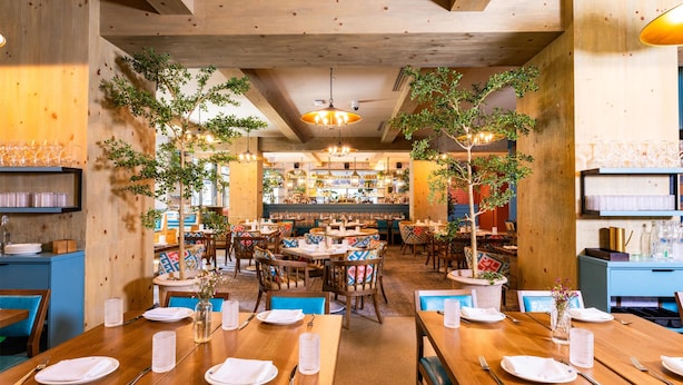 Ein Restaurant mit Holztischen und -stühlen, Pflanzen und hängenden Lampen.