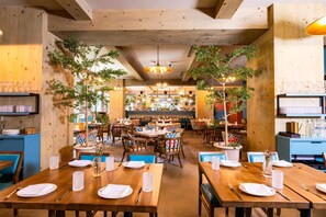 Een restaurant met houten tafels en stoelen, planten en hangende lampen.
