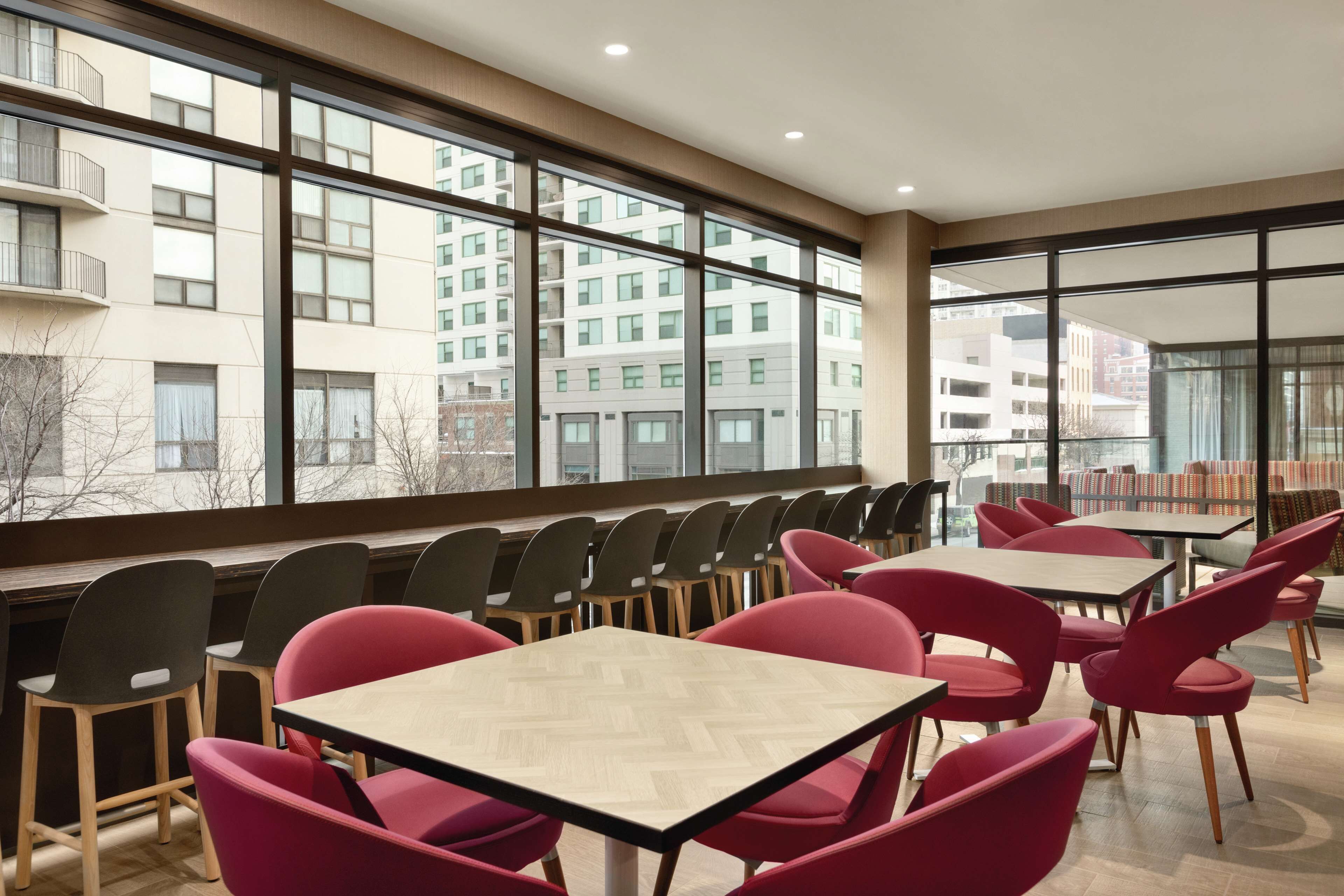 A modern dining area with large windows, multiple tables, and chairs.