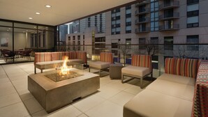 Ein Außen-Loungesbereich mit Feuerstelle, Sitzgelegenheiten und Blick auf hohe Gebäude.