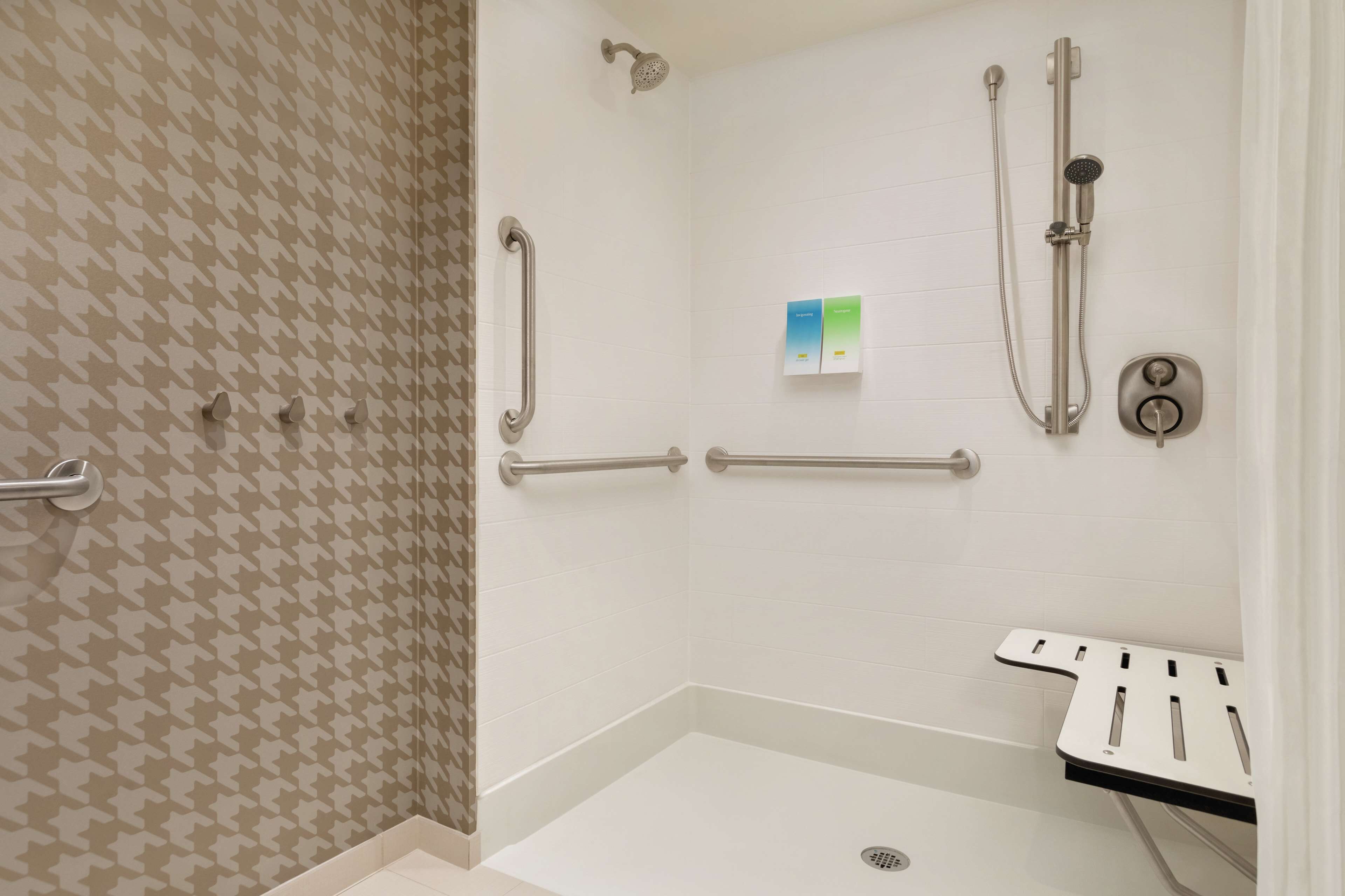 A shower area with a handrail, a handheld showerhead, a wall-mounted showerhead, and a control panel.